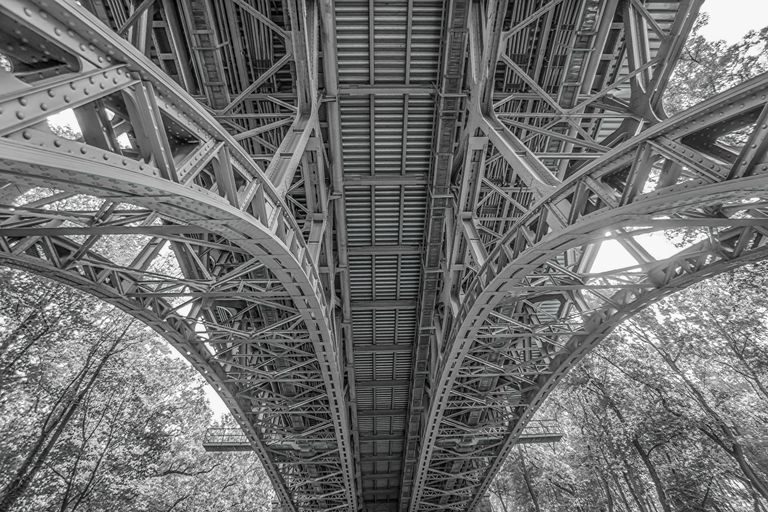 The interconnected beams and supports beneath a bridge revealing the structure that makes the visible outcome defensible.