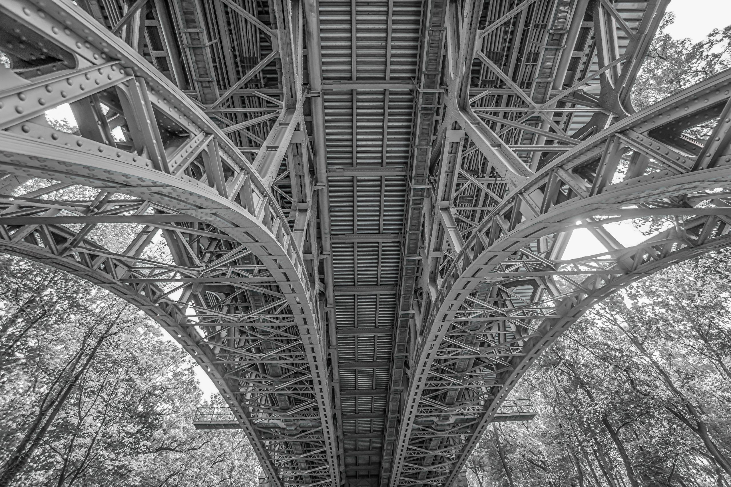 The interconnected beams and supports beneath a bridge revealing the structure that makes the visible outcome defensible.