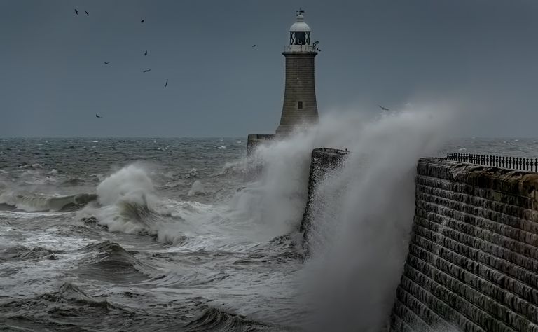 An established breakwater and lighthouse absorbing the force of a storm before it reaches the harbour.